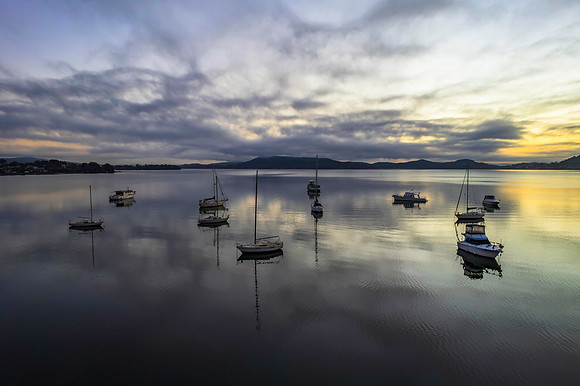 Sunrise waterscape with boats, soft clouds and reflections