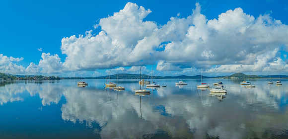 Aerial panorama over the bay with clouds, reflections and boats