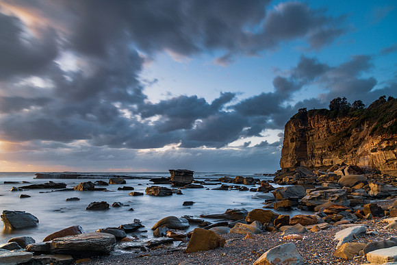 Moody sunrise seascape with clouds at the rocky inlet