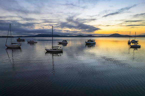 Sunrise waterscape with boats, soft clouds and reflections
