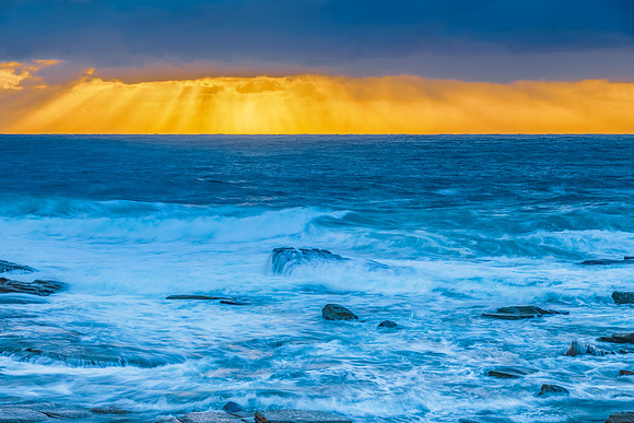 Moody sunrise seascape with clouds and sunrays at the rocky inle