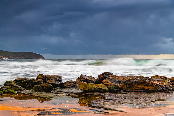 Sunrise at the seaside with rocks and rain clouds