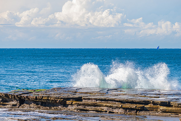 Morning seascape at rocky inlet with clouds and sailboats