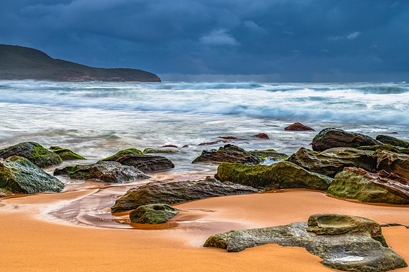 Sunrise at the seaside with rocks and rain clouds