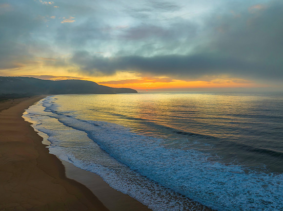 Peaceful sunrise over the ocean with small waves and clouds