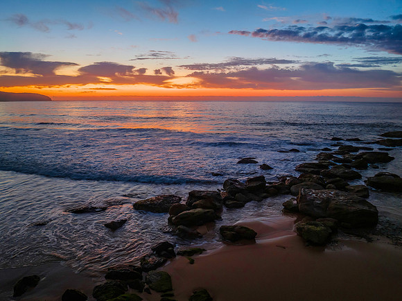 Orange dawn breaks over the ocean with small waves and clouds