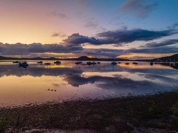 Aerial sunrise waterscape with boats, rain clouds and reflection