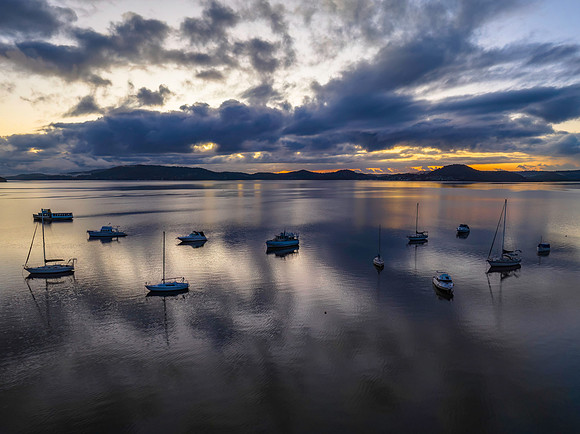 Aerial sunrise waterscape with boats, rain clouds and reflection
