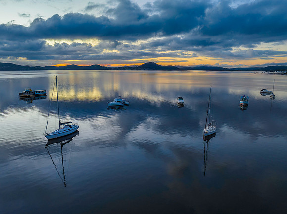 Aerial sunrise waterscape with boats, rain clouds and reflection