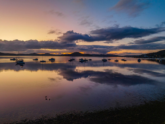 Aerial sunrise waterscape with boats, rain clouds and reflection