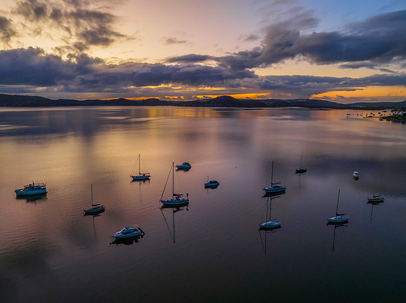Aerial sunrise waterscape with boats, rain clouds and reflection