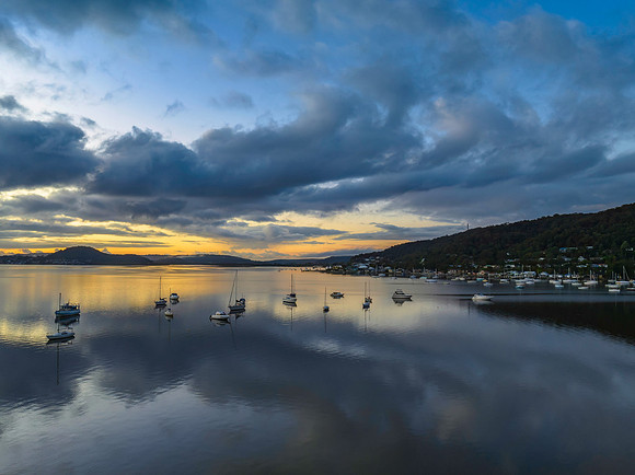 Aerial sunrise waterscape with boats, rain clouds and reflection
