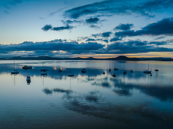 Aerial sunrise waterscape with boats, rain clouds and reflection