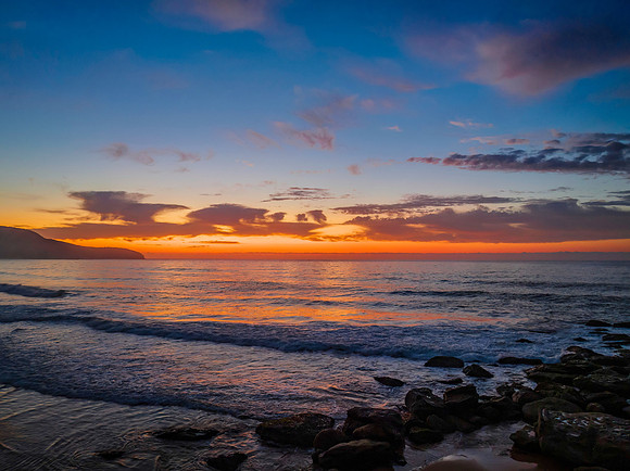 Orange dawn breaks over the ocean with small waves and clouds