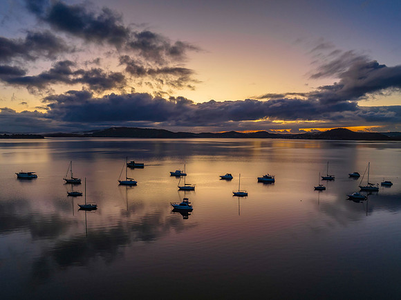 Aerial sunrise waterscape with boats, rain clouds and reflection