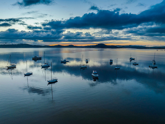 Aerial sunrise waterscape with boats, rain clouds and reflection