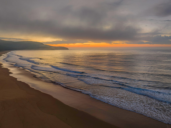Peaceful sunrise over the ocean with small waves and clouds