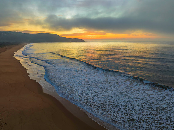 Peaceful sunrise over the ocean with small waves and clouds