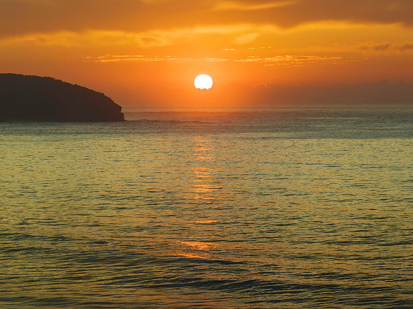 Peaceful sunrise over the ocean with small waves and clouds