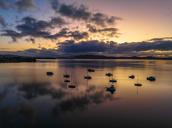 Aerial sunrise waterscape with boats, rain clouds and reflection