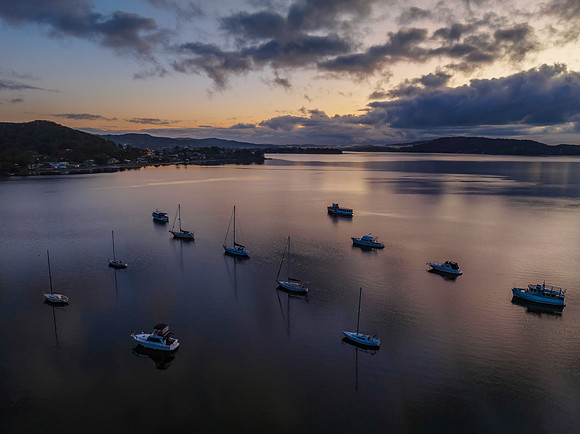 Aerial sunrise waterscape with boats, rain clouds and reflection