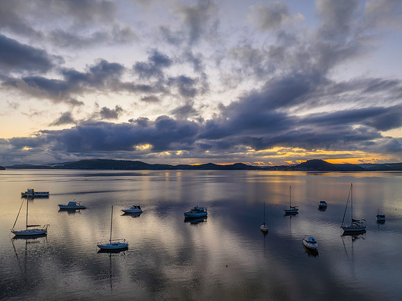 Aerial sunrise waterscape with boats, rain clouds and reflection