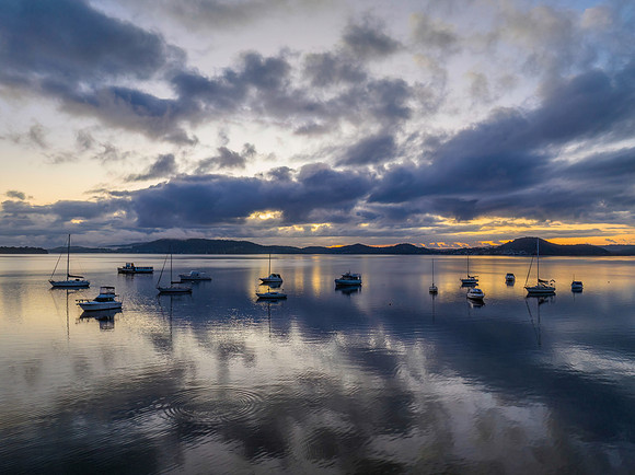 Aerial sunrise waterscape with boats, rain clouds and reflection