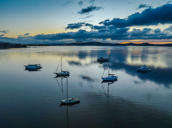 Aerial sunrise waterscape with boats, rain clouds and reflection