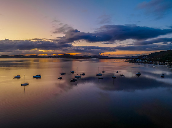 Aerial sunrise waterscape with boats, rain clouds and reflection