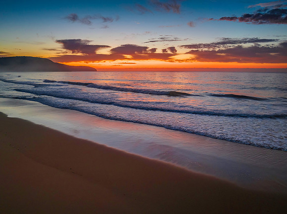 Orange dawn breaks over the ocean with small waves and clouds