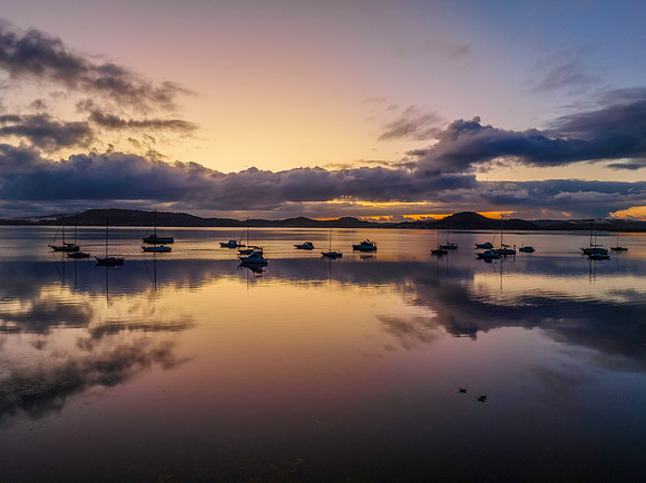 Aerial sunrise waterscape with boats, rain clouds and reflection