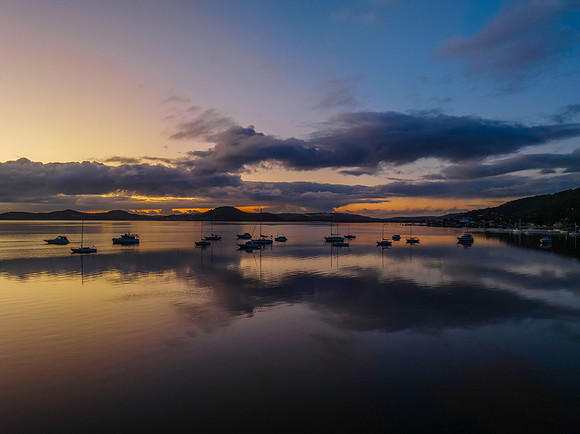 Aerial sunrise waterscape with boats, rain clouds and reflection