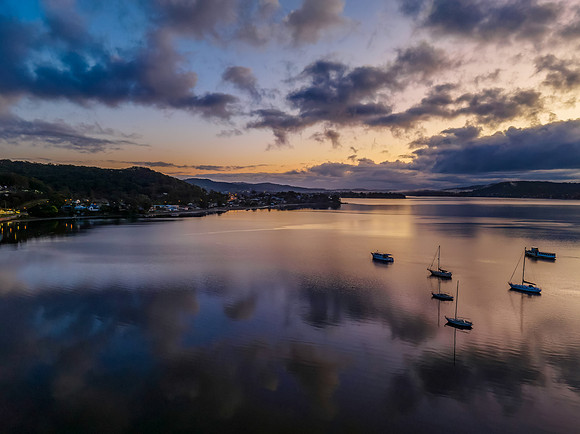 Aerial sunrise waterscape with boats, rain clouds and reflection