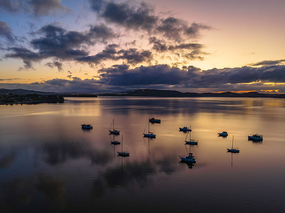 Aerial sunrise waterscape with boats, rain clouds and reflection