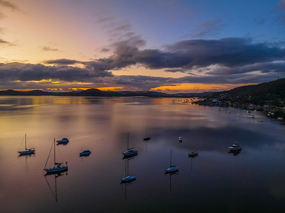 Aerial sunrise waterscape with boats, rain clouds and reflection