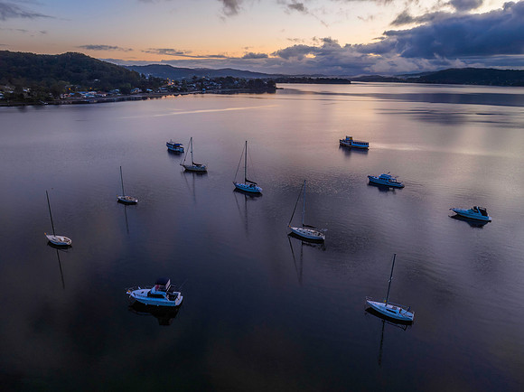 Aerial sunrise waterscape with boats, rain clouds and reflection