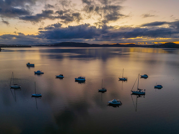 Aerial sunrise waterscape with boats, rain clouds and reflection