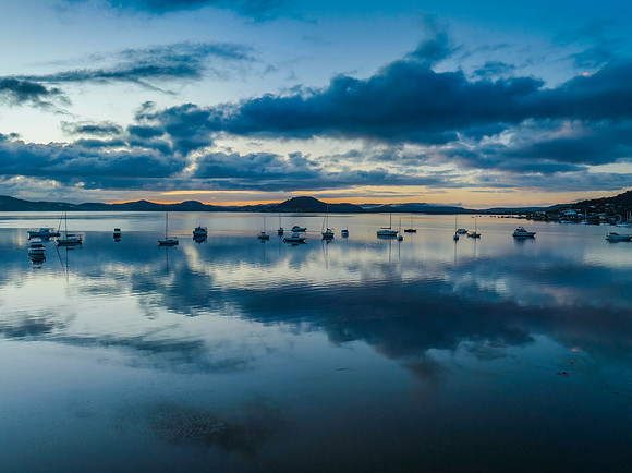 Aerial sunrise waterscape with boats, rain clouds and reflection