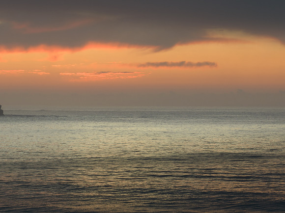 Peaceful sunrise over the ocean with small waves and clouds