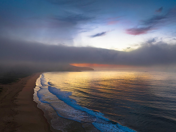Peaceful sunrise over the ocean with small waves, clouds and fog