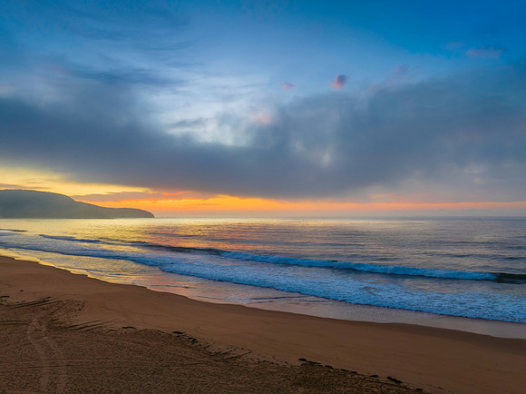 Peaceful sunrise over the ocean with small waves and clouds