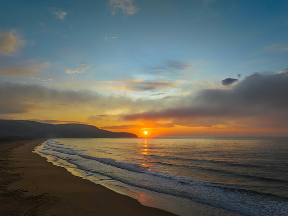 Peaceful sunrise over the ocean with small waves and clouds
