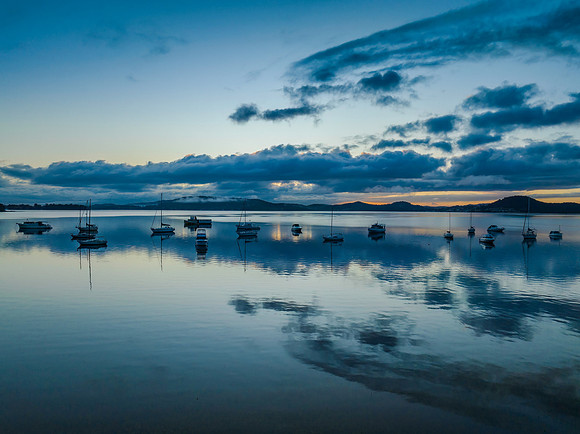 Aerial sunrise waterscape with boats, rain clouds and reflection