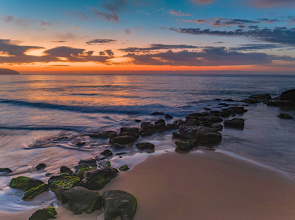 Peaceful sunrise over the ocean with small waves and clouds