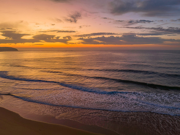 Peaceful sunrise over the ocean with small waves and clouds