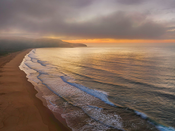 Peaceful sunrise over the ocean with small waves and clouds