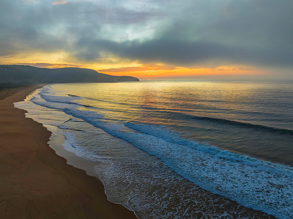 Peaceful sunrise over the ocean with small waves and clouds