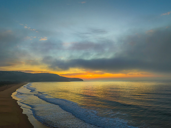 Peaceful sunrise over the ocean with small waves and clouds