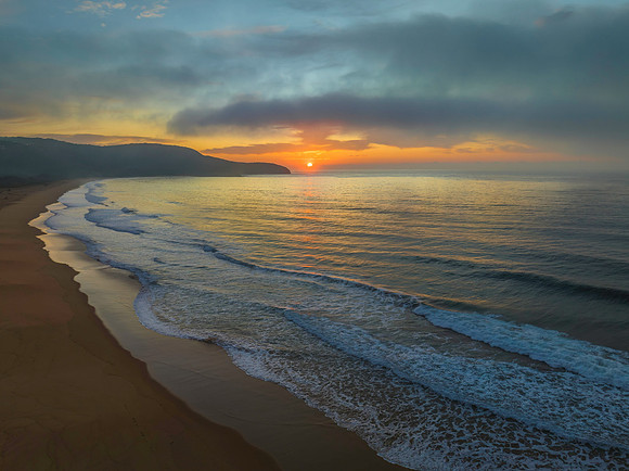 Peaceful sunrise over the ocean with small waves and clouds