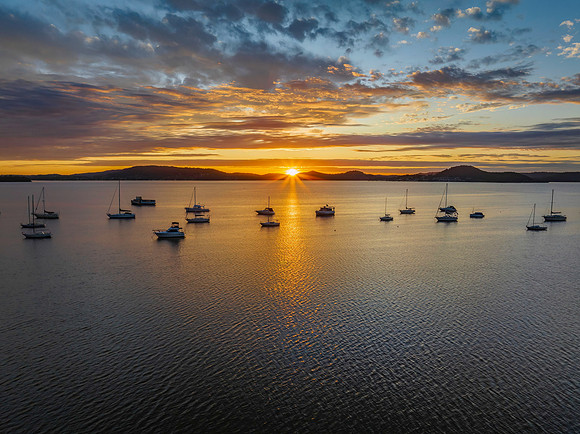 Aerial sunrise over the bay with boats, clouds and sunburst
